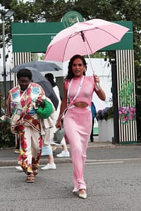 Saffron Hocking walking to Wimbledon in a 2 piece matching top and skirt and a coordinating pink umbrella.