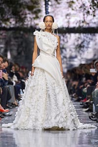 Model Walks Runway in Dior Couture show in white gown with draped bodice and floral skirt.