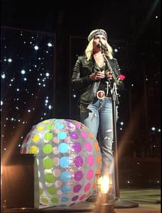 Miranda Lambert singing at a mic stand with a fan's beachball to the left on stage with her.