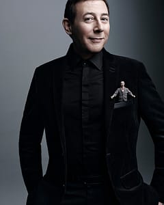 Paul Reubens with a small Pee-Wee Herman plush stuffed in his suit jacket pocket.