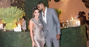 Khloé Kardashian (left) grinning at the camera with Tristan Thompson (right)kissing her head with his arm around her