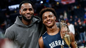 Lebron James (left) posing with his arm over his son Bronny James (right) who is holding a trophy after winning a basketball game