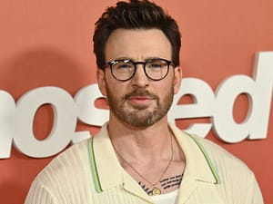 Chris Evans doing press for his film 'Ghosted'. He's in a white cardigan with small teal, yellow and green stripes lining the collar.