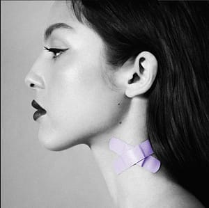 Olivia Rodrigo's single cover for 'Vampire'. She's facing left wearing dark lipstick, winged eyeliner, and her dark hair is pushed back behind her ears. The photo is in black and white except for two lavender bandaids on her neck. They're crossed over each other to make and X shape.