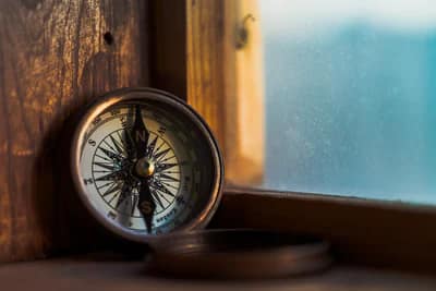 brown, classic compass located on a window sill with a blue background.