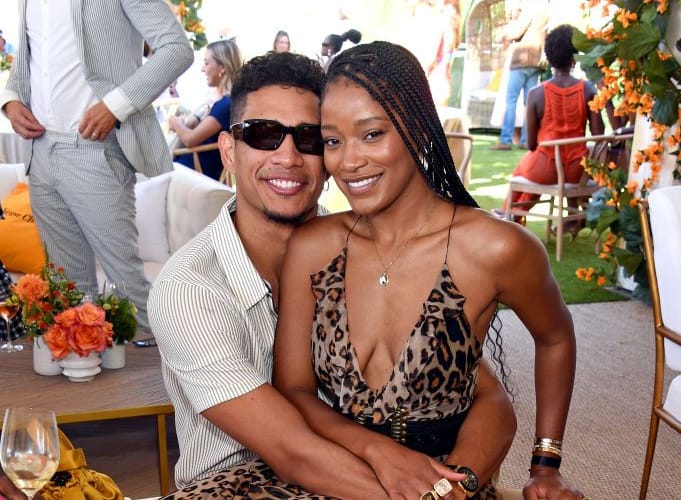 Keke Palmer sitting on Darius Jackson's lap. She is wearing a deep cut leopard-print dress, and he is in a white short-sleeved collared shirt.