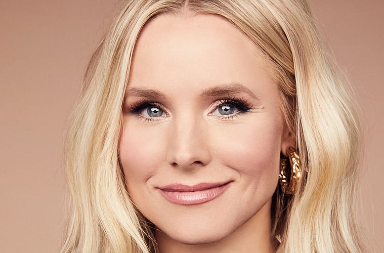 A headshot of Kristen Bell grinning in front if an ombre peach/light pink background.
