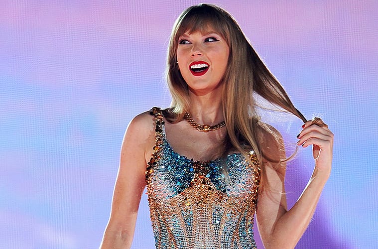 A close up photo of Taylor Swift on stage at The Eras Tour. She's wearing the 'Lover' bodysuit and is twirling her hair in her left hand.