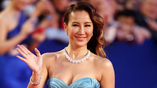 Coco Lee walking down a red carpet in a baby blue, off the shoulder, satin dress and a diamond necklace.