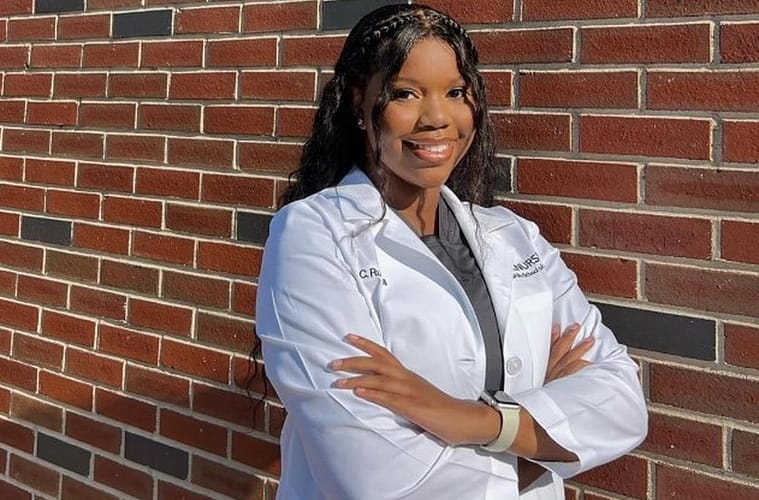 Carlee Russell in her nursing student uniform posing with her arms crossed leaning against a red brick wall