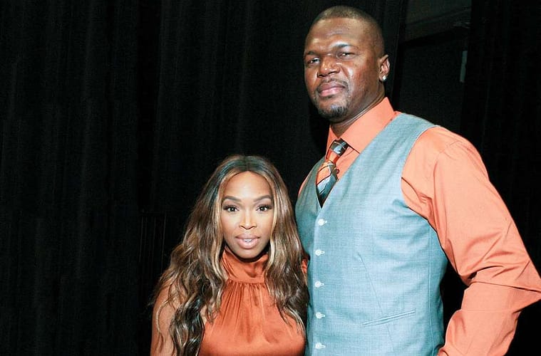 Khadijah Haqq (left) and Bobby McCray (right) posing for a photo together in front of a black velvet curtain backstage at an event