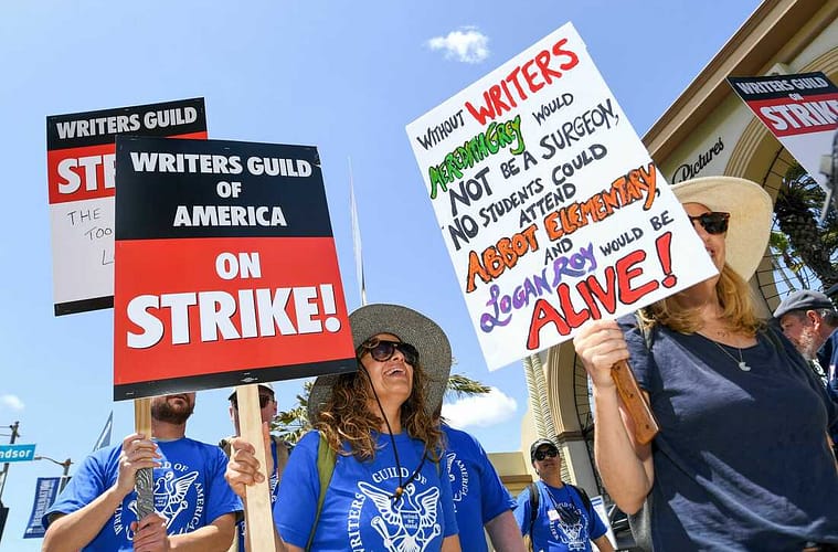 A picketer at Paramount Studios in Los Angeles carries a sign with references to the television shows Grey's Anatomy, Abbott Elementary and Succession
