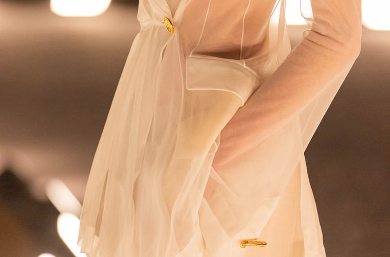 A sheer ivory Schiaparelli suit from the Spring/Summer 2026 runway, featuring a translucent tailored jacket with gold hardware and soft, fluid draping.